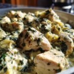 Close-up of tender chicken pieces coated in a rich, creamy sauce with spinach and artichoke hearts in a skillet.