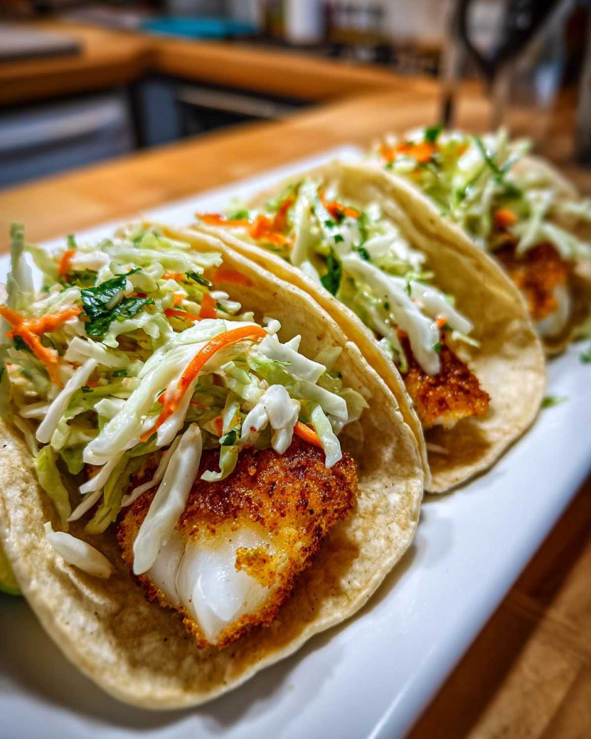Three Crispy Baked Fish Tacos topped with bright lime slaw, served on a white platter.