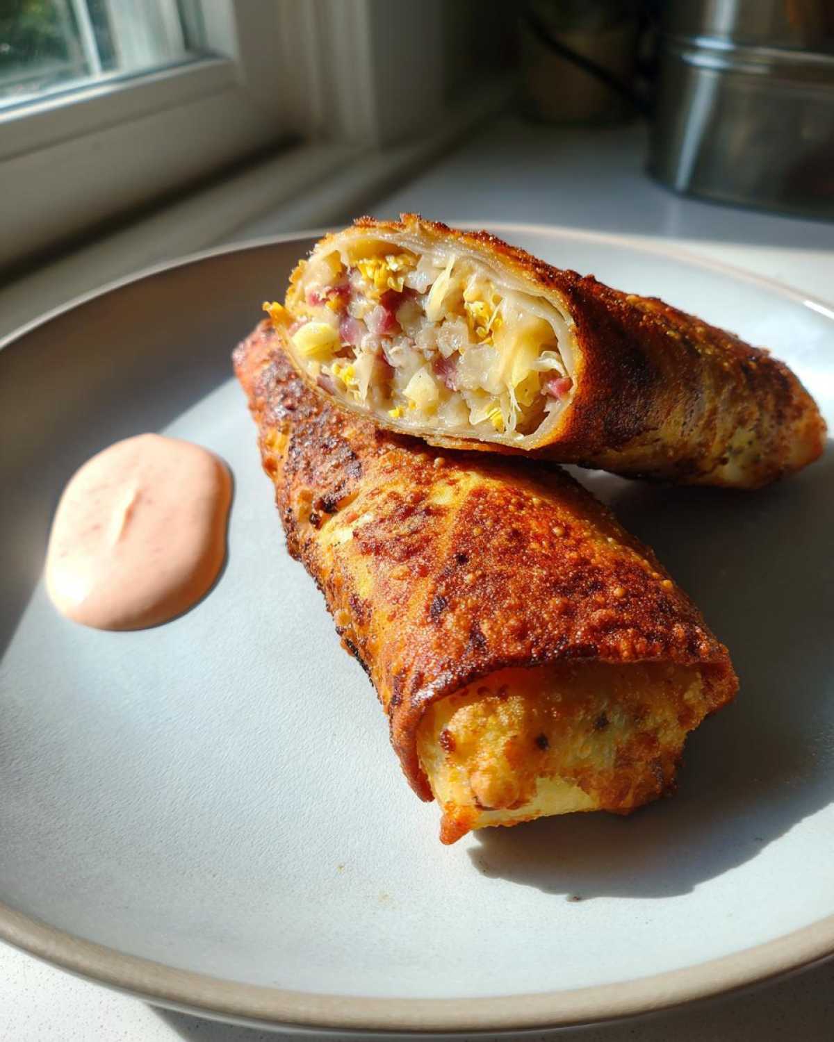 Two Crispy Baked Reuben Egg Rolls, one cut in half showing corned beef and sauerkraut filling, served with Thousand Island dip.