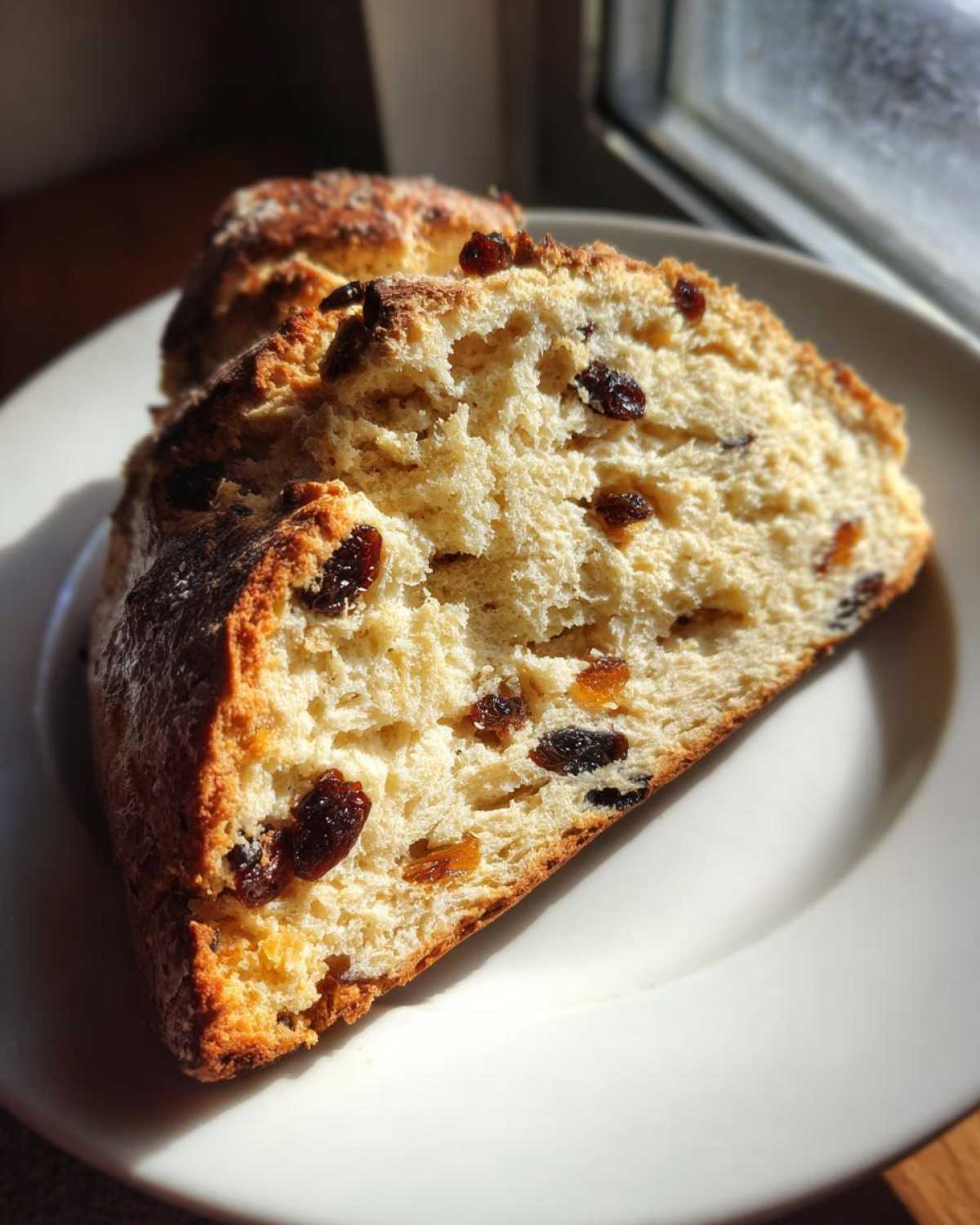 Close-up of a thick slice of Easy Irish Soda Bread with Buttermilk and Raisins on a white plate.
