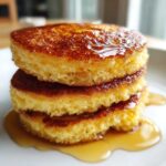 Close-up of three thick Gluten-Free Buttermilk Pancakes stacked and drizzled with golden syrup.