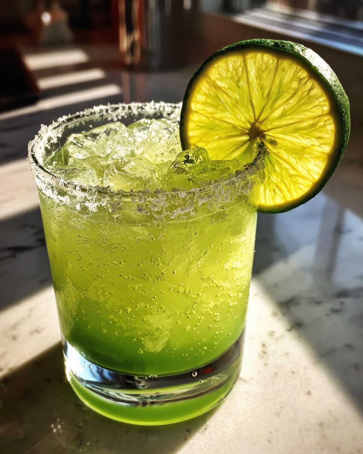 Close-up of a bright green Fresh Jalapeño Lime Margarita with crushed ice and a backlit lime wheel garnish.