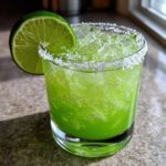 Close-up of a bright green Fresh Jalapeño Lime Margarita, filled with crushed ice and garnished with a lime wheel and salt rim.