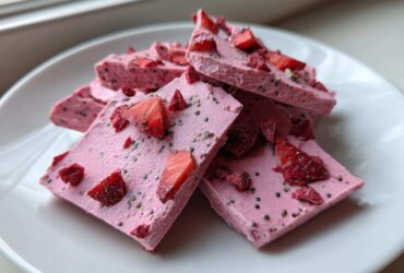 Close-up of stacked pieces of bright pink Frozen Strawberry Yogurt Bark topped with fresh and dried strawberries and chia seeds.