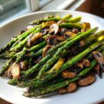 A close-up of vibrant green Garlic Butter Roasted Asparagus and Mushrooms served on a white plate.