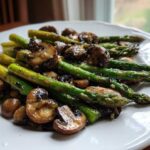 Close-up of vibrant green Garlic Butter Roasted Asparagus and Mushrooms served on a white plate.