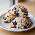 Three delicious Blueberry Lemon Scones stacked on a white plate, drizzled with white lemon glaze.