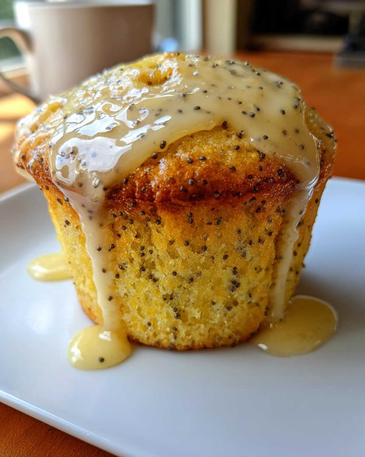 A single Glazed Lemon Poppy Seed Muffin topped with thick, dripping lemon glaze and visible poppy seeds.