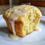 Close-up of a Glazed Lemon Poppy Seed Muffin with icing dripping onto a white plate.