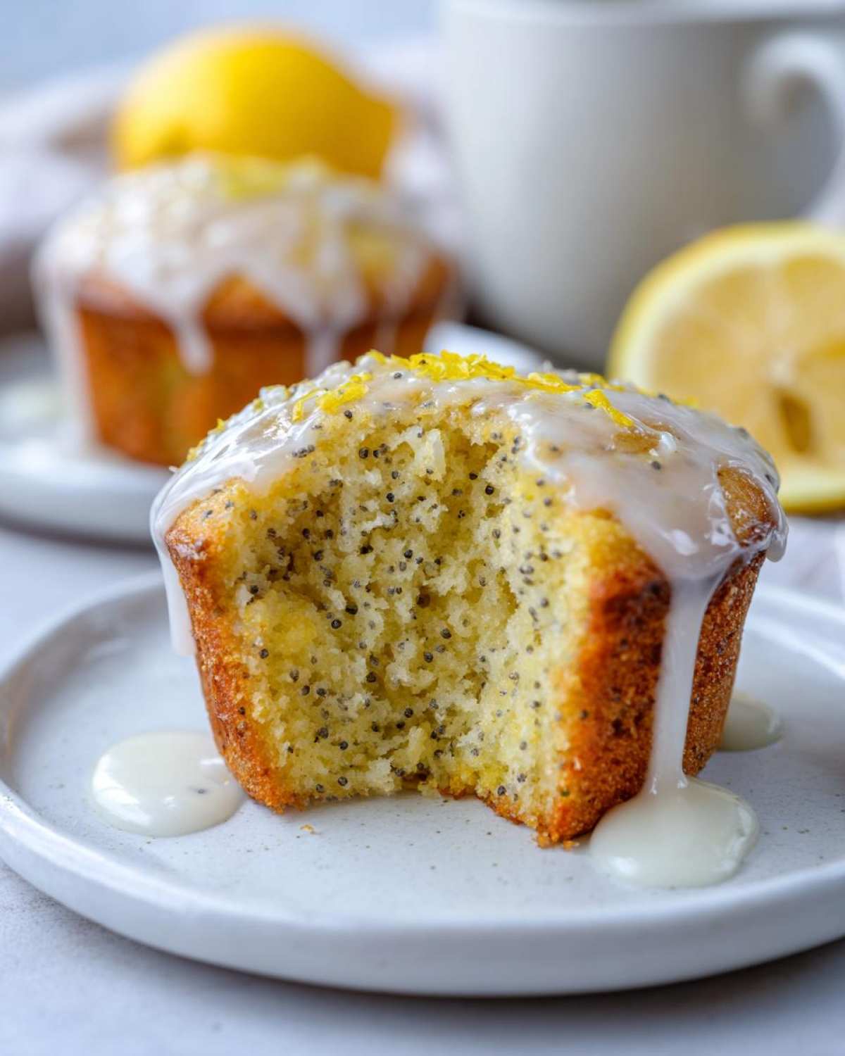 A Glazed Lemon Poppy Seed Muffin with a bite taken out, showing the moist interior and poppy seeds, drizzled with lemon glaze.
