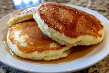 Close-up of three fluffy Gluten-Free Buttermilk Pancakes stacked and drizzled generously with golden syrup.