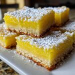 Close-up of several Gluten-Free Lemon Bars with Shortbread Crust dusted heavily with powdered sugar on a white plate.