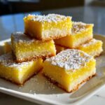 A stack of bright yellow Gluten-Free Lemon Bars with shortbread crust dusted generously with powdered sugar.