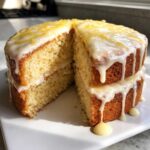 A two-layer Gluten-Free Lemon Coconut Cake with white lemon glaze dripping down the sides, served on a white plate.