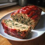 Close-up of a slice cut from a Healthy Turkey Spinach Meatloaf topped with a bright red glaze.