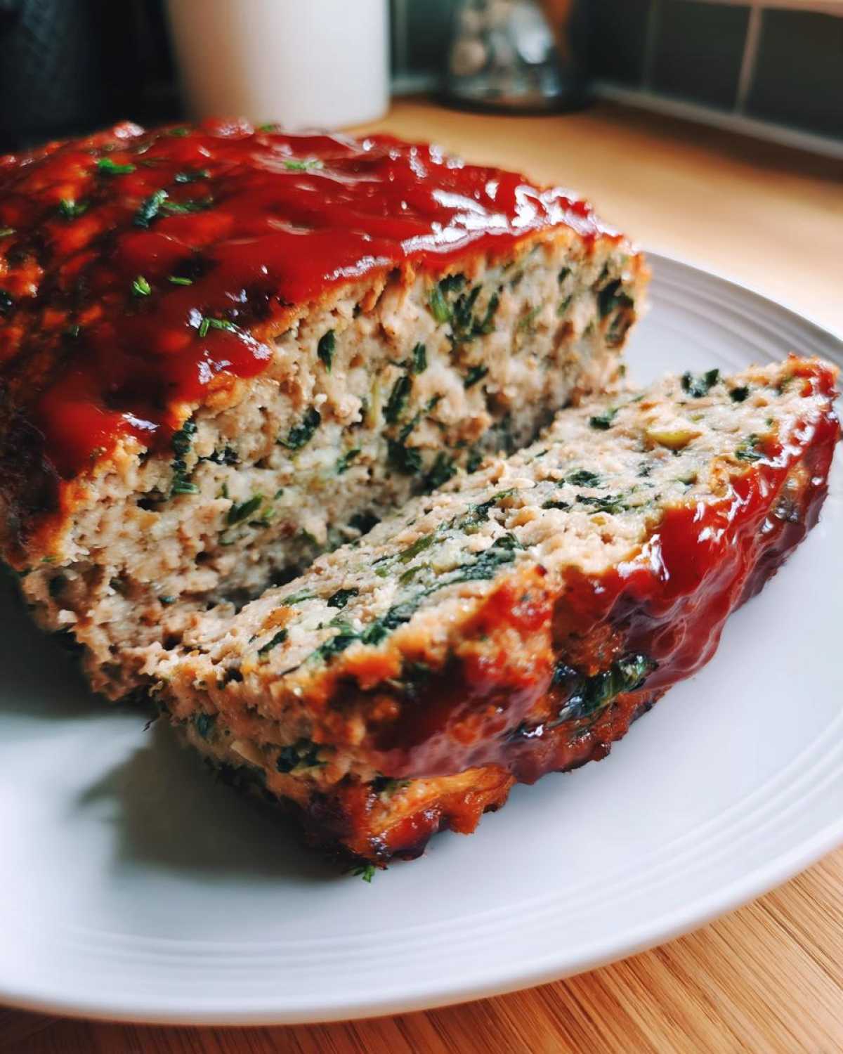A close-up of a slice cut from a Healthy Turkey Spinach Meatloaf, topped with a shiny red glaze.