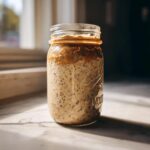 A jar filled with High-Protein Peanut Butter Overnight Oats, topped with a layer of peanut butter.