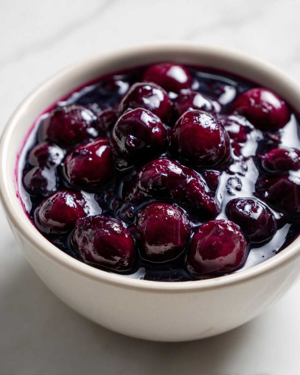 Close-up of plump blueberries suspended in thick, dark sauce, ready to be served as Homemade Blueberry Syrup.