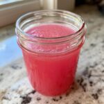 Close-up of bright pink Homemade Strawberry Lemonade Concentrate filling a small glass jar.