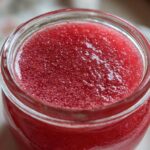Close-up of vibrant red Homemade Strawberry Lemonade Concentrate filling a glass jar.