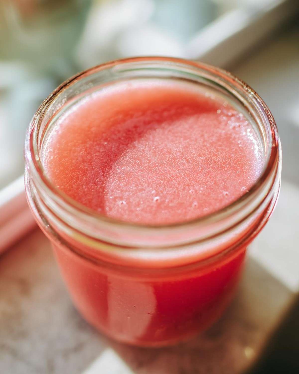 Close-up of bright pink Homemade Strawberry Lemonade Concentrate filling a small glass jar.