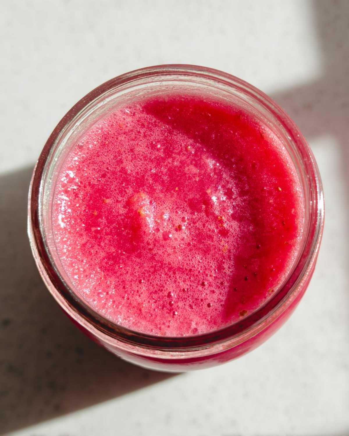 Overhead view of vibrant pink Homemade Strawberry Lemonade Concentrate filling a glass jar.