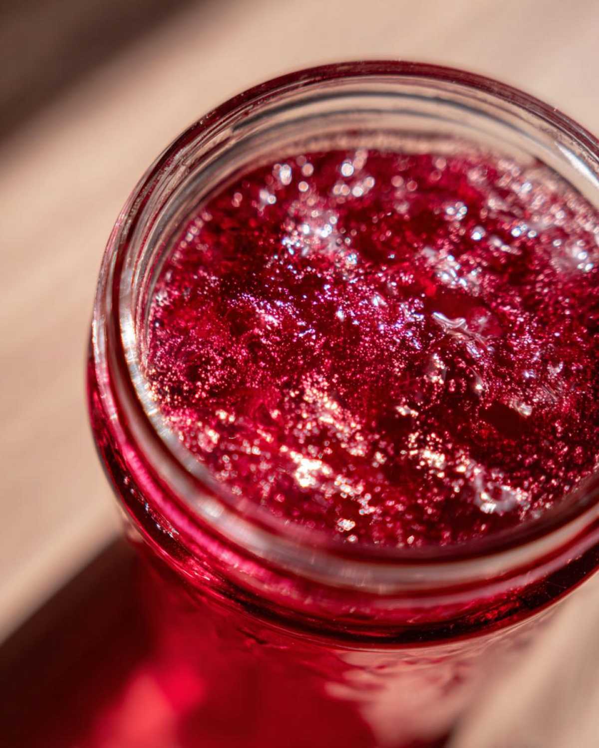 Top-down close-up of vibrant red Homemade Strawberry Lemonade Concentrate in a glass jar, showing texture and light reflection.