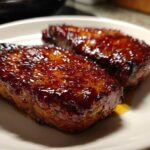 Close-up of two glistening Honey Glazed Ham Steak in the Skillet pieces on a white plate.