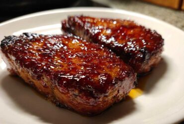 Close-up of two glistening Honey Glazed Ham Steak in the Skillet pieces on a white plate.