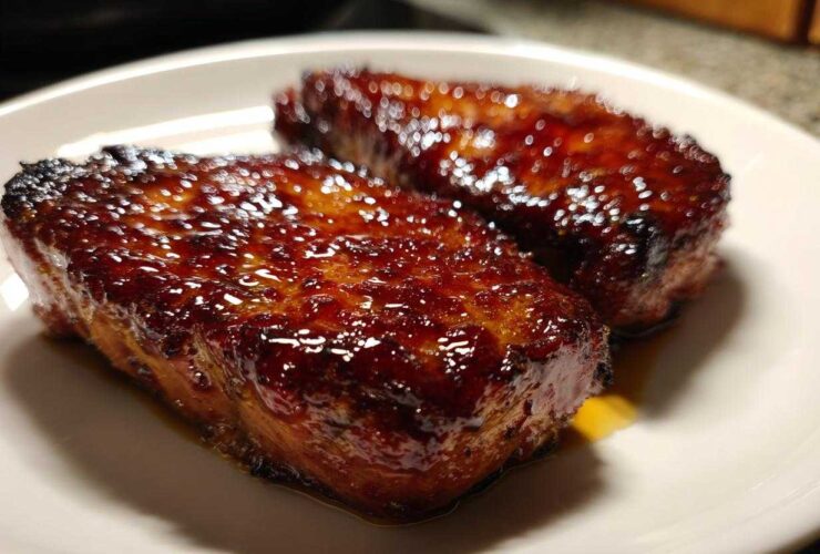 Close-up of two glistening Honey Glazed Ham Steak in the Skillet pieces on a white plate.