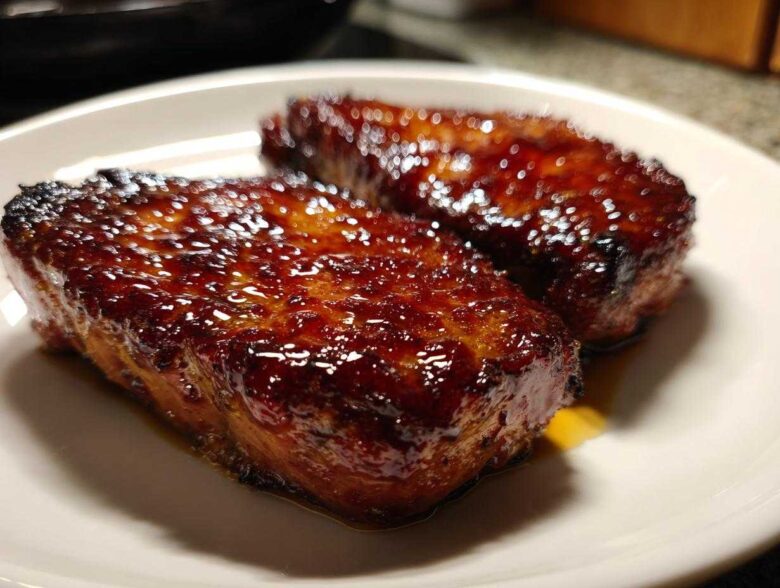 Close-up of two glistening Honey Glazed Ham Steak in the Skillet pieces on a white plate.