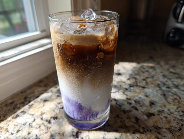 Close-up of a tall glass containing a layered Iced Lavender Latte with purple syrup, milk, espresso, and ice.