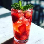 Close-up of a tall glass filled with Iced Strawberry Lemon Tea, ice, sliced strawberries, and a mint garnish.