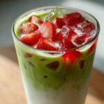 Close-up of a vibrant Iced Strawberry Matcha Latte layered with milk, green matcha, and topped with ice and sliced fresh strawberries.
