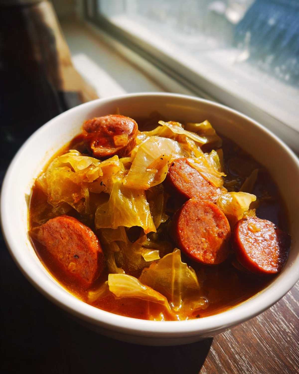 Close-up of a white bowl filled with Instant Pot Cabbage and Sausage Soup, featuring thick sausage slices and cooked cabbage.