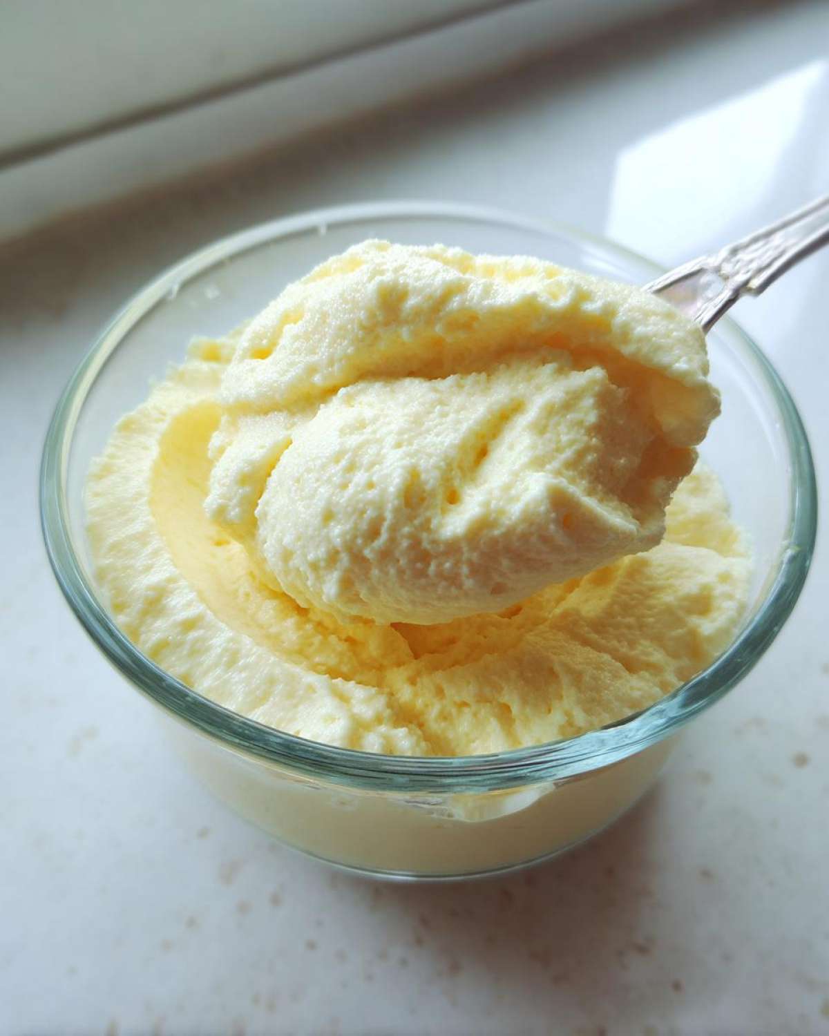A spoonful of light, airy Keto Lemon Cheesecake Mousse being lifted from a small glass bowl.