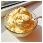 A spoonful of light yellow Keto Lemon Cheesecake Mousse being lifted from a glass bowl.