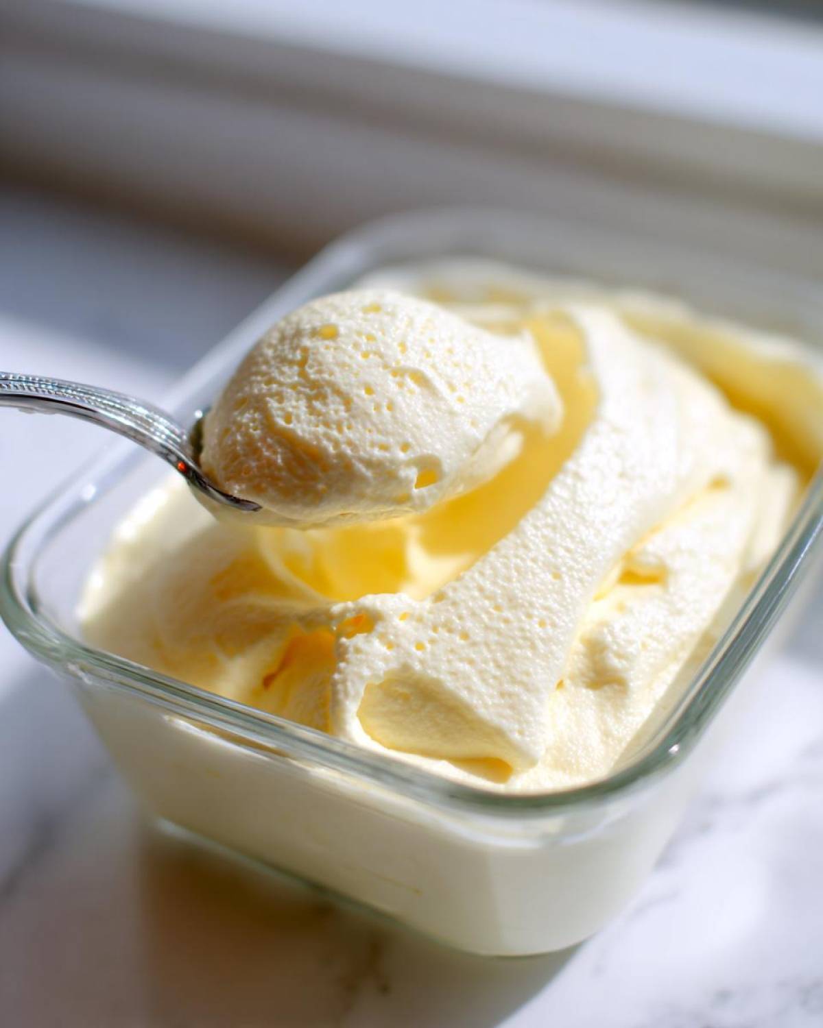 A spoonful of light and airy Keto Lemon Cheesecake Mousse being lifted from a glass dish.
