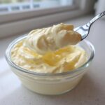 A spoonful of light yellow Keto Lemon Cheesecake Mousse being lifted from a small glass bowl.