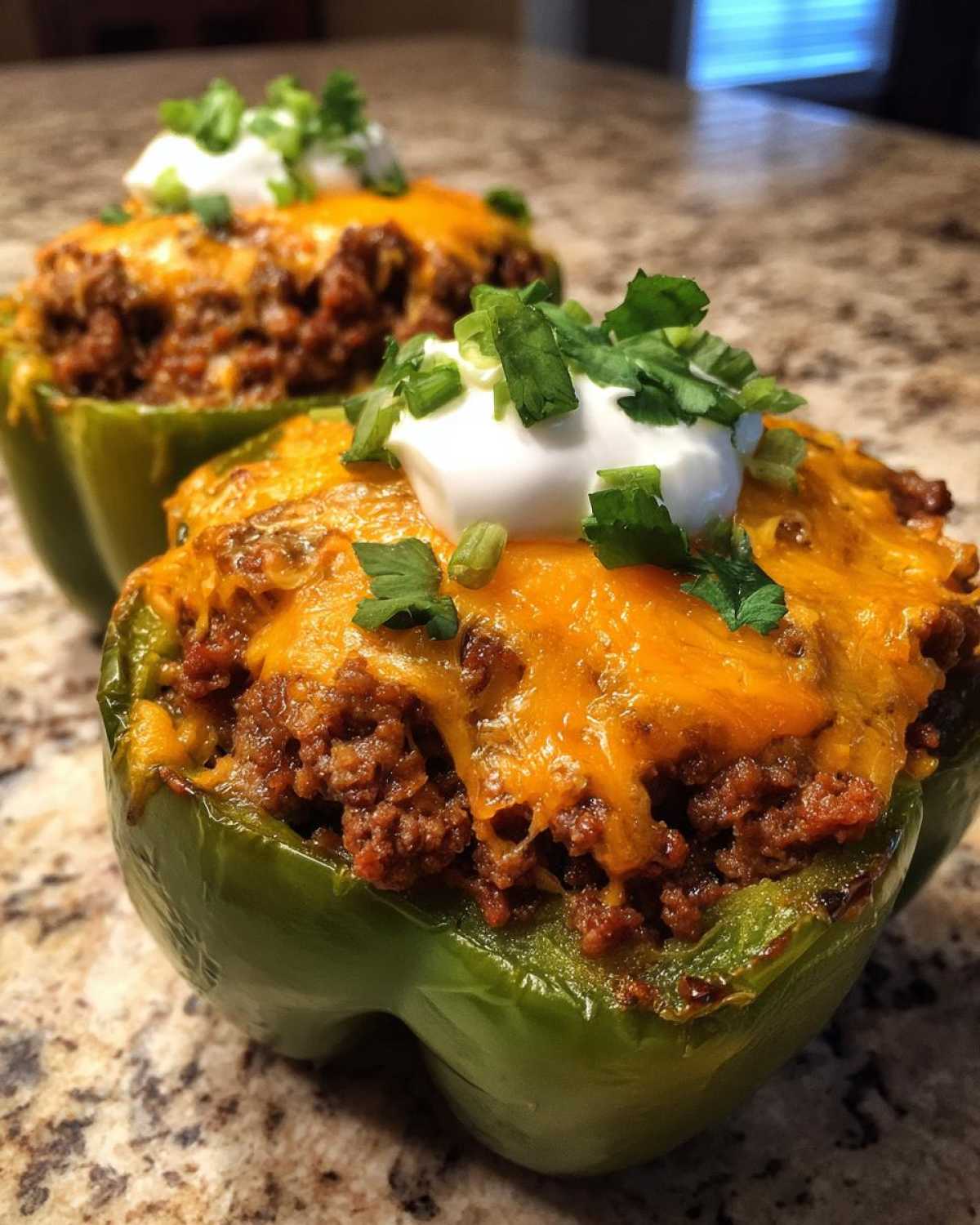 Close-up of two Keto Taco Stuffed Peppers filled with seasoned ground beef, topped with melted cheddar cheese, sour cream, and cilantro.
