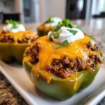 Close-up of a green bell pepper filled with seasoned ground beef, melted cheddar cheese, sour cream, and cilantro, representing Keto Taco Stuffed Peppers.