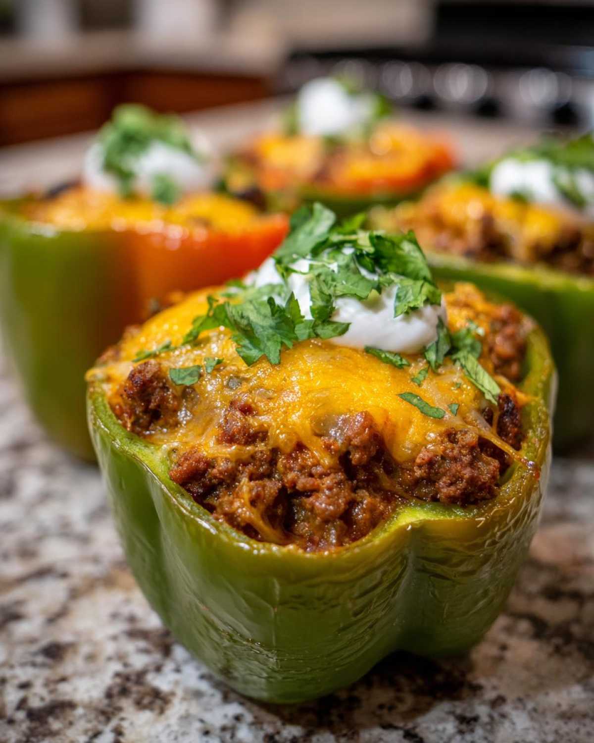 A close-up of a vibrant green Keto Taco Stuffed Pepper filled with seasoned ground meat, melted cheddar cheese, and topped with sour cream and cilantro.