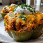 Close-up of two Keto Taco Stuffed Peppers topped with melted cheddar cheese, sour cream, and cilantro.