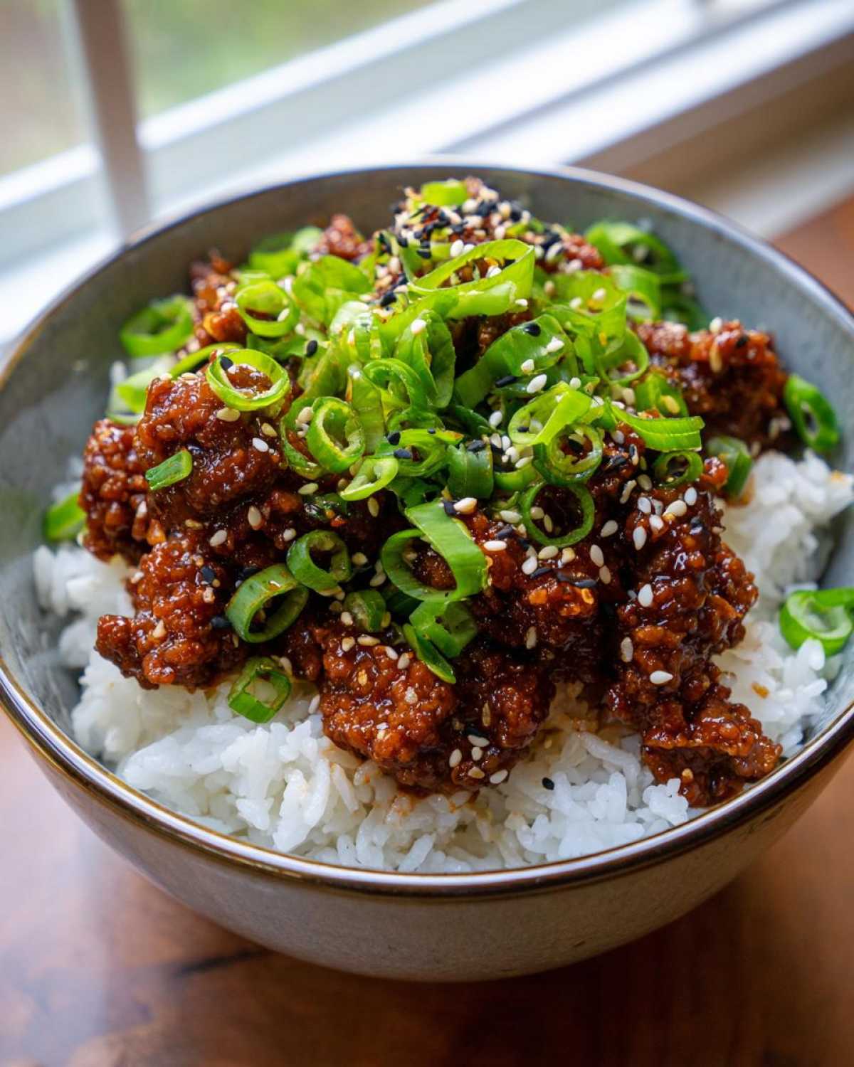 Close-up of a Korean Ground Beef Bulgogi Bowl topped generously with sliced green onions and sesame seeds over white rice.