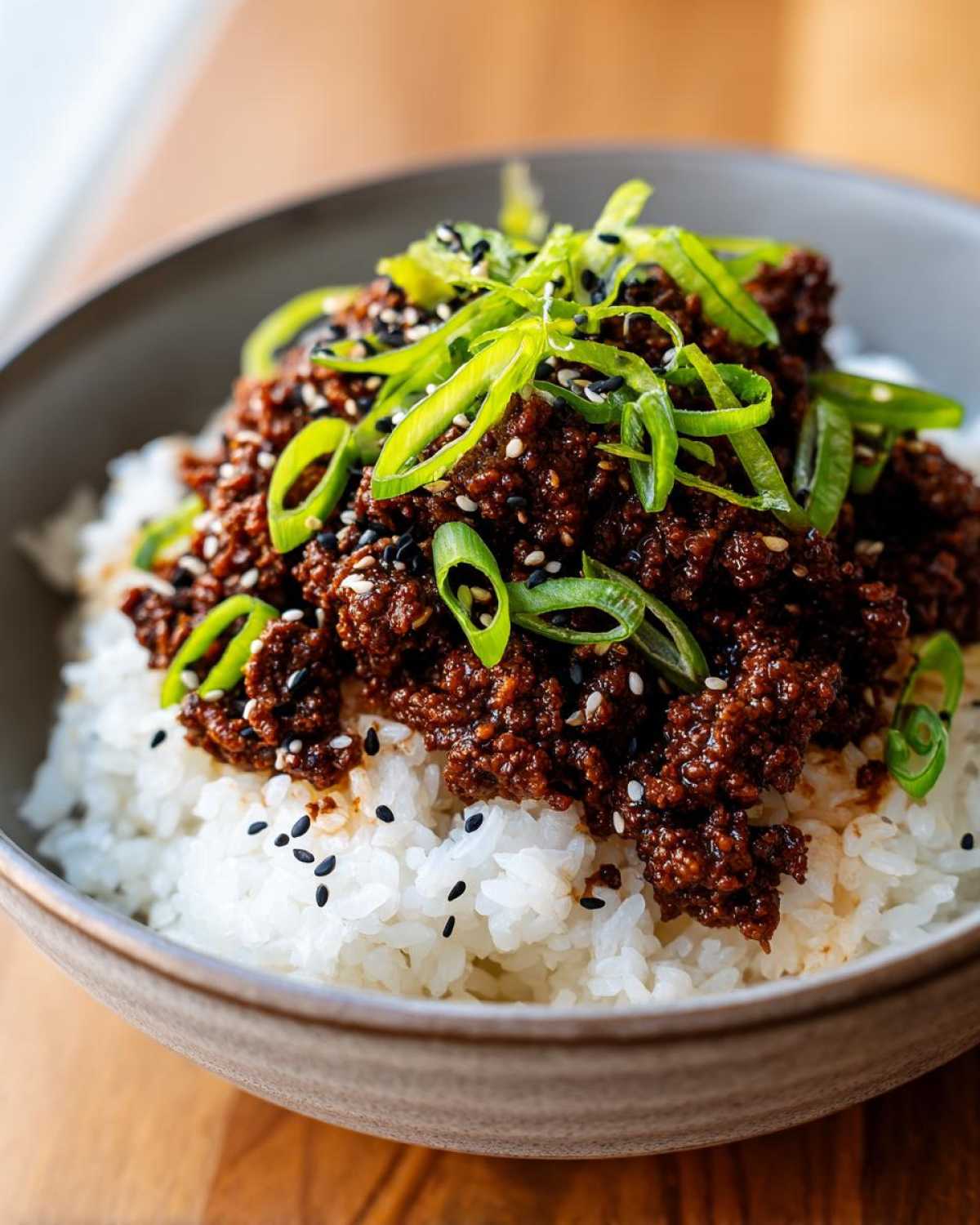 A close-up of a bowl of Korean Ground Beef Bulgogi Bowls, topped with green onions and sesame seeds over white rice.