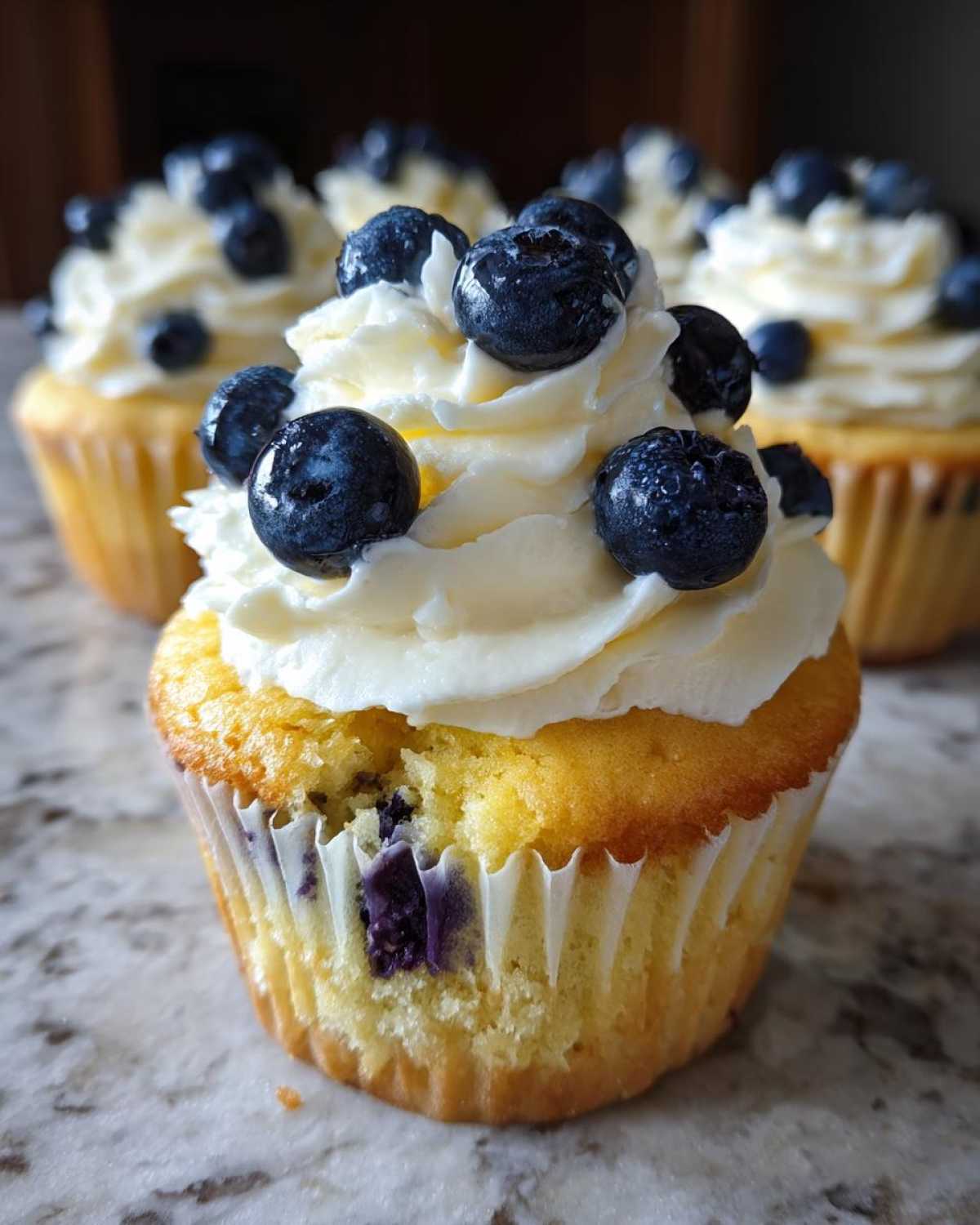 A close-up of a Lemon Blueberry Cupcakes with Cream Cheese Frosting, topped with fresh blueberries.