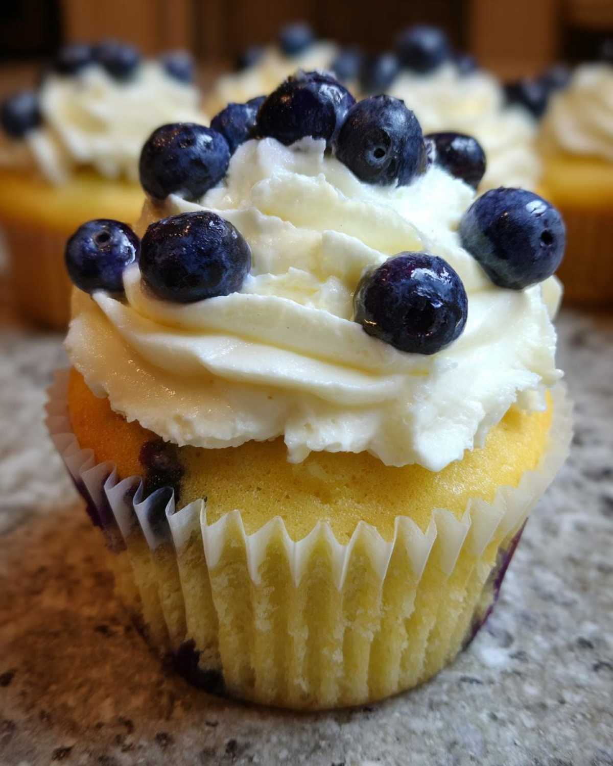 A close-up of a Lemon Blueberry Cupcake with thick cream cheese frosting topped with fresh blueberries.