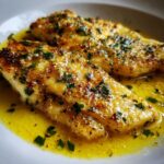 Two pan-seared Lemon Garlic Butter Tilapia fillets swimming in bright yellow butter sauce and topped with fresh parsley.