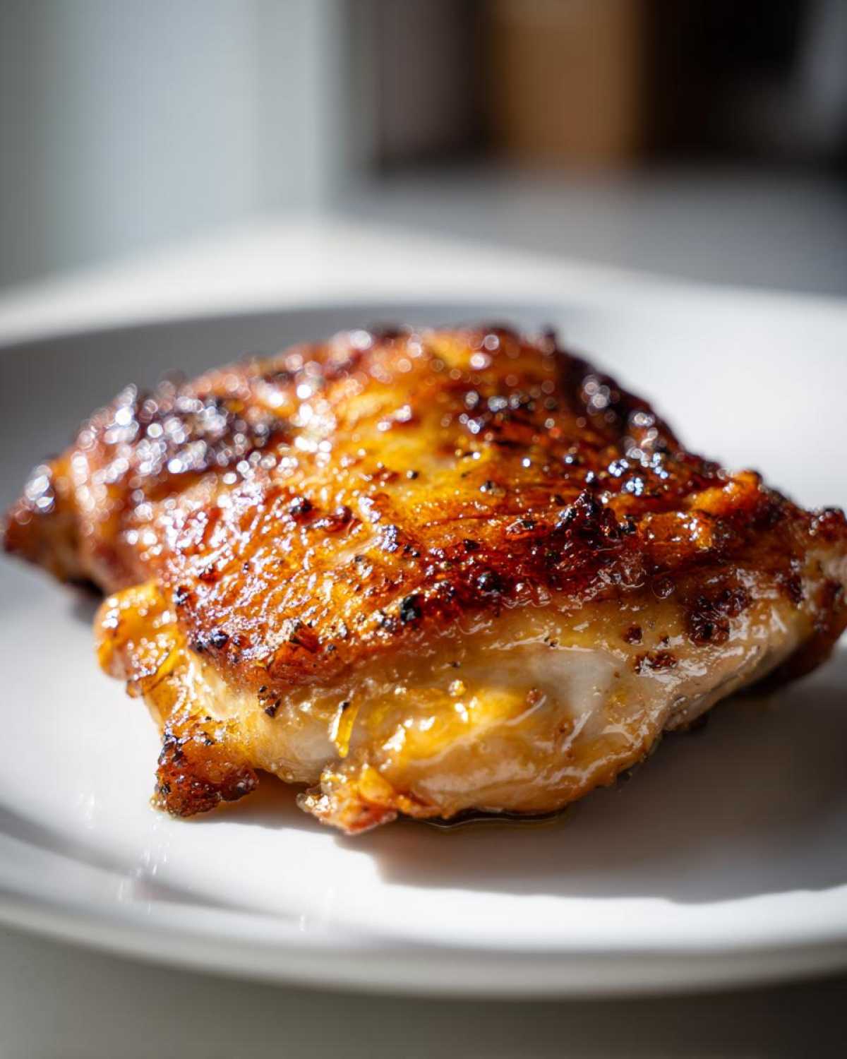 Close-up of a juicy, caramelized Lemon Garlic Roasted Chicken Thigh on a white plate.