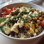 A vibrant Mediterranean Quinoa Bowl topped with chickpeas, cucumbers, tomatoes, feta, and drizzled with lemon tahini sauce.
